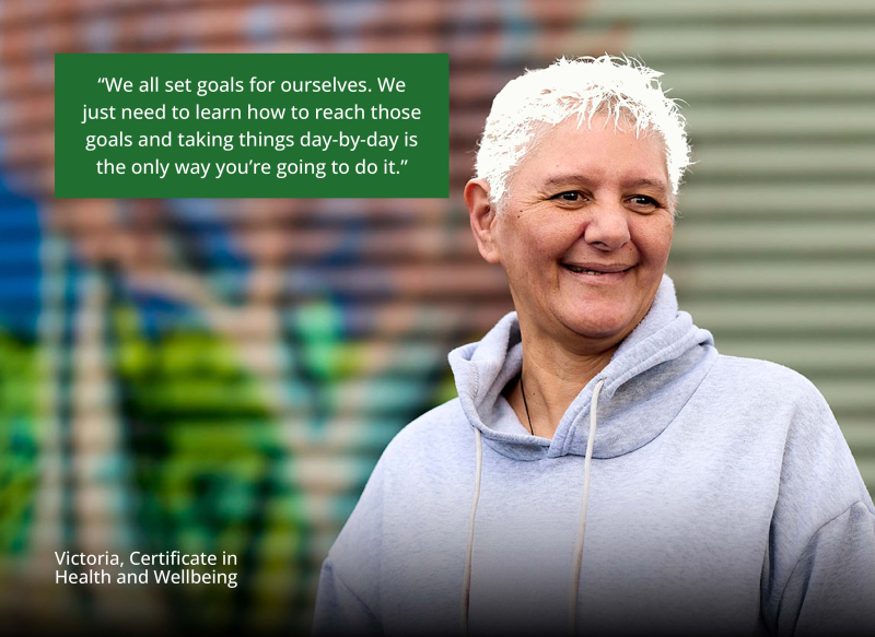 Victoria stands at her workplace in front of a colourful mural, smiling. Quote reads: “We all set goals for ourselves. We just need to learn how to reach those goals and taking things day-by-day is the only way you're going to do it.” – Victoria, Certific