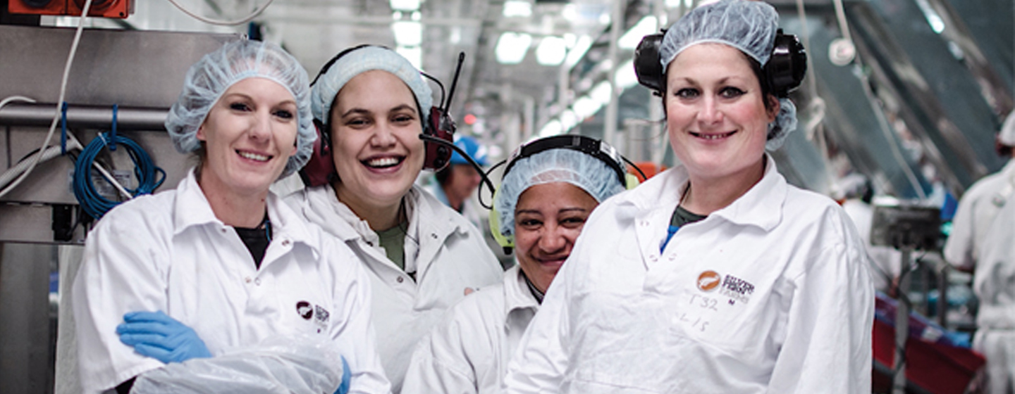 Four women smiling in protective gear in factory